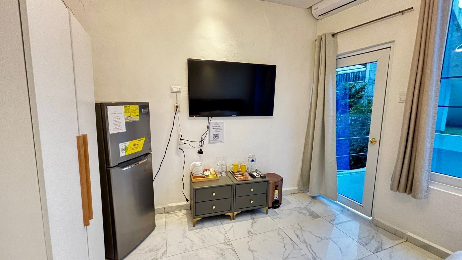 Une cuisine compacte équipée d’un réfrigérateur, d’un four à micro-ondes et d’un petit placard. Un téléviseur à écran plat est fixé au mur, au-dessus du comptoir.
