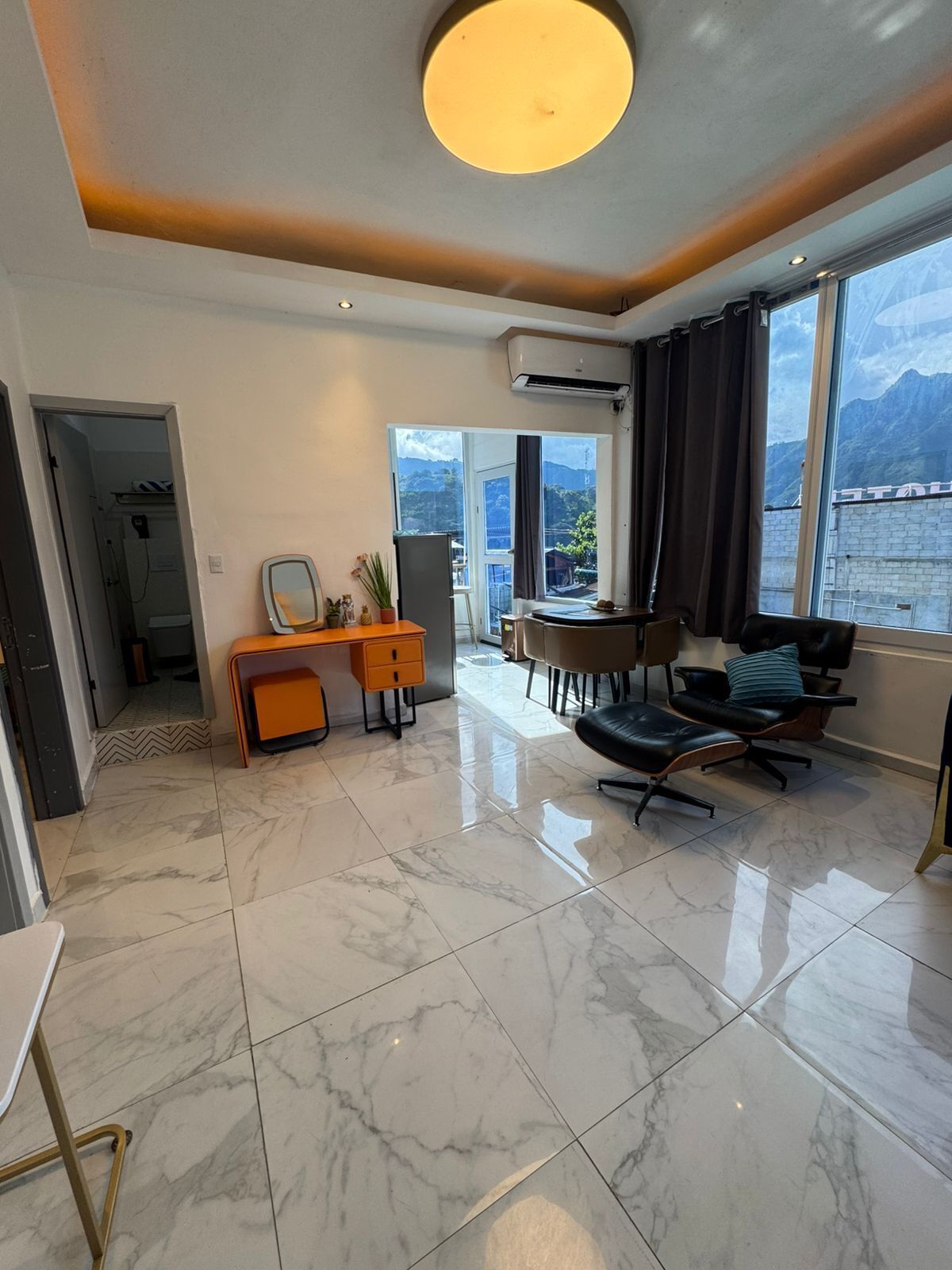 A modern living room with a large window, a dining area, and a view of mountains.