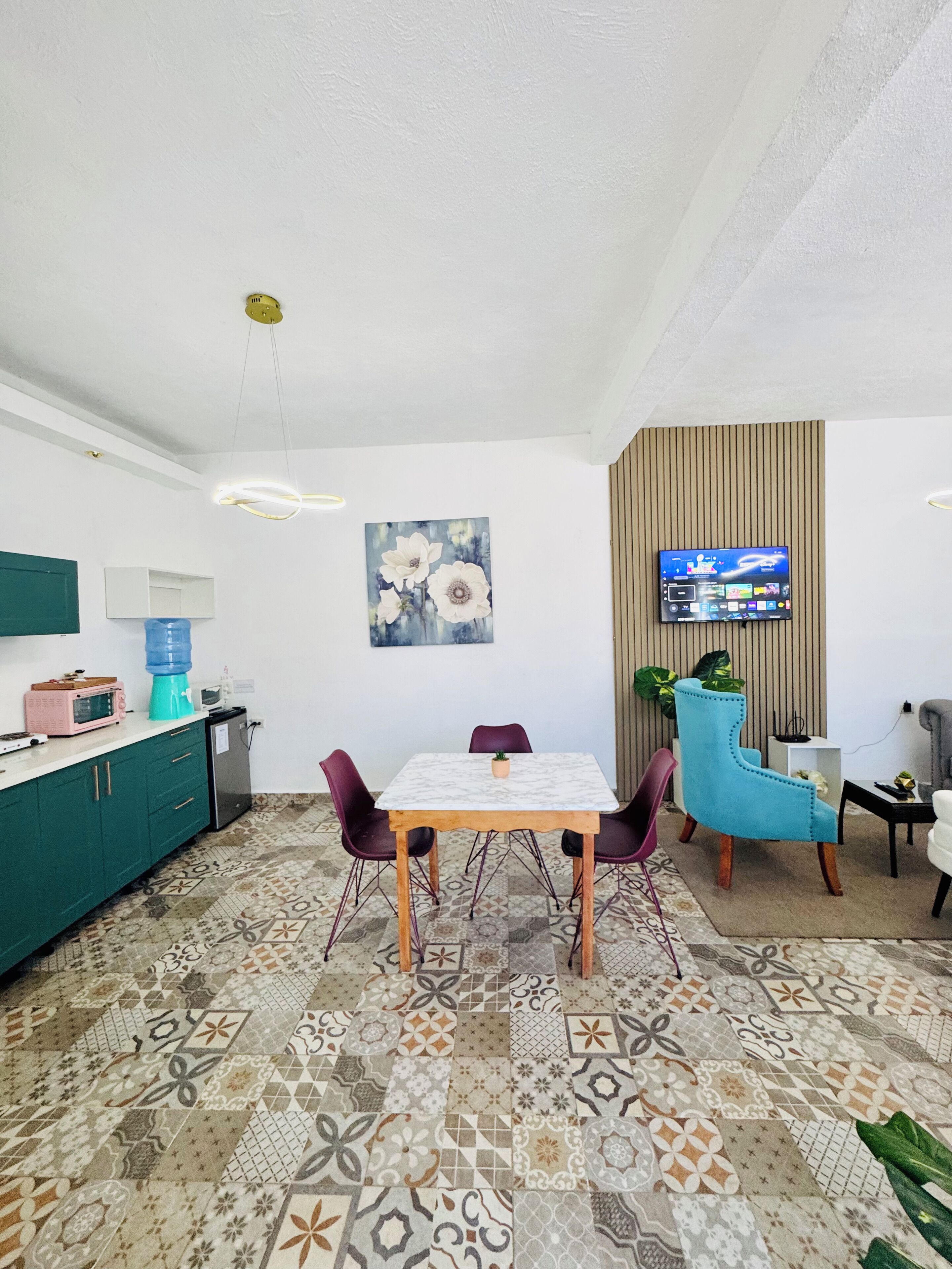 Una cocina moderna con comedor, suelo de baldosas, televisor montado en la pared y dispensador de agua.