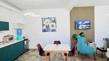 Una cocina moderna con comedor, suelo de baldosas, televisor montado en la pared y dispensador de agua.