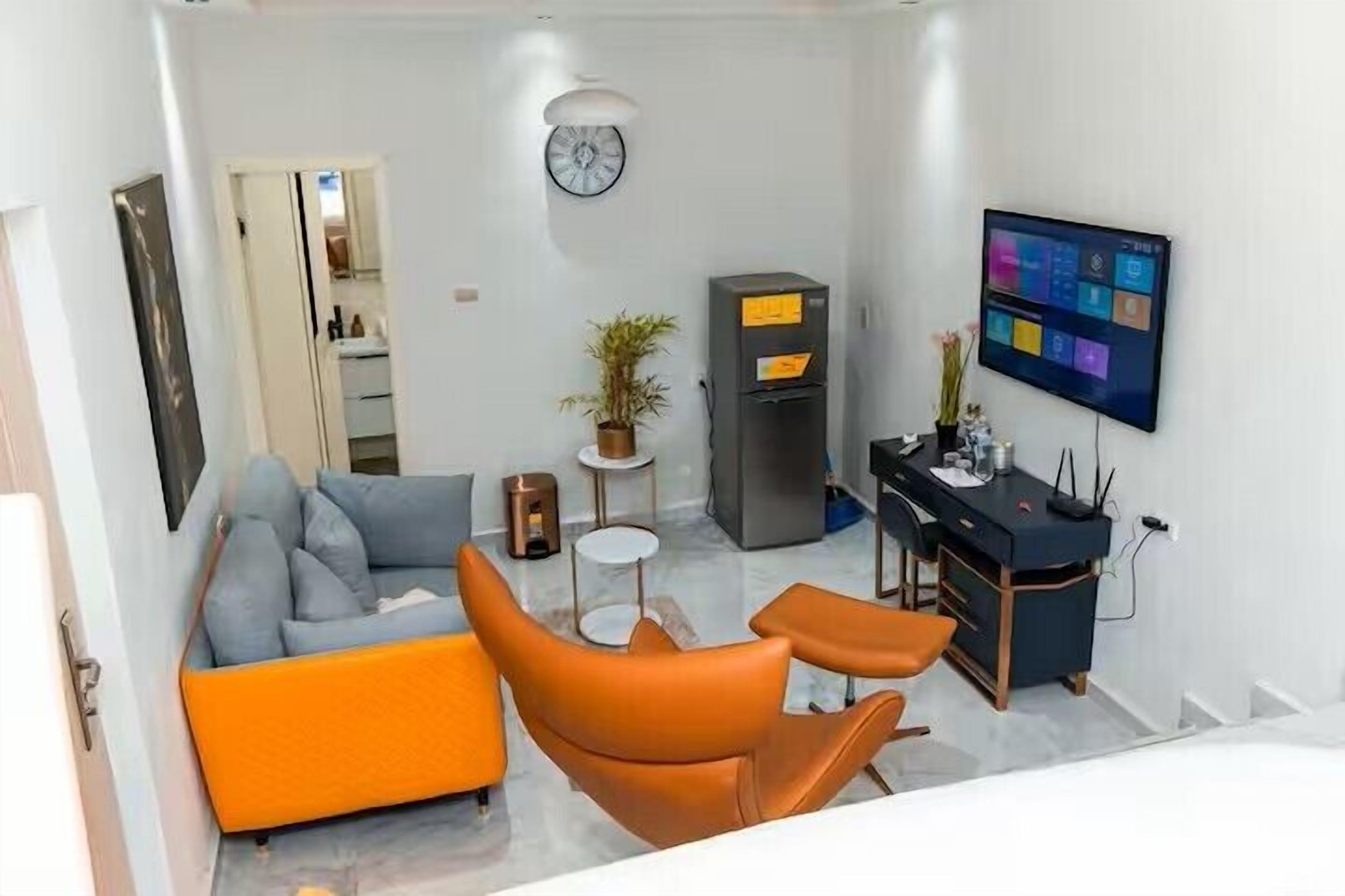 Un soggiorno moderno con un divano, poltrone, un tavolino, una TV e un frigorifero.