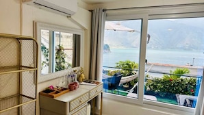 Varanda com vista para um lago e montanhas, uma mesa pequena com uma cadeira e uma janela com cortinas.
