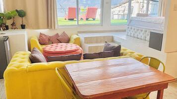 Una habitación luminosa con un sofá amarillo, una mesa de madera y vistas a montañas a través de amplios ventanales.