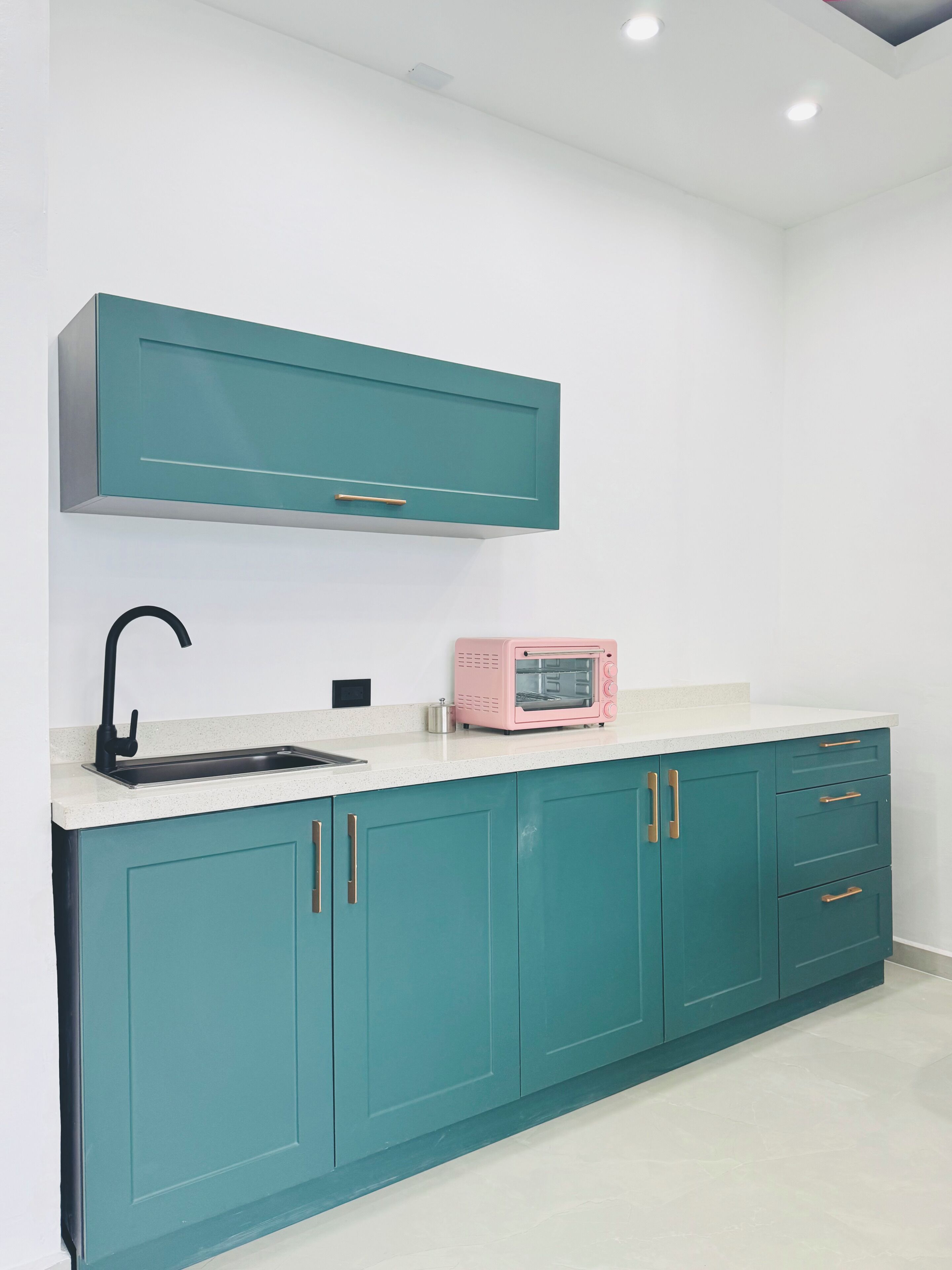 A kitchen with teal cabinets, a white countertop, a black faucet, and a pink microwave.