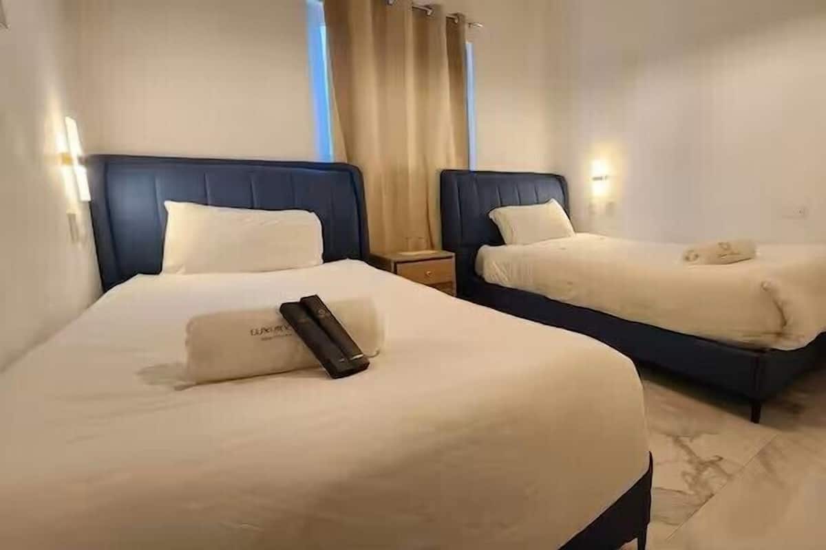 Two beds with headboards, a bedside table, and a lamp on each bed.