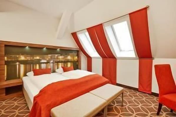 A bedroom with a large bed, a bench, a chair, and a window with curtains. - H+ Hotel Lübeck (Lubeck)