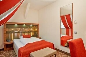 A hotel room with a bed, a mirror, a chair, and a headboard with a cityscape view. - H+ Hotel Lübeck (Lubeck)