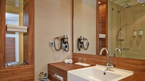 A modern bathroom with a large mirror, a sink, and a shower area. - H+ Hotel Lübeck (Lubeck)