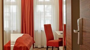 A hotel room with a bed, a chair, a table, and a window with curtains. - H+ Hotel Lübeck (Lubeck)