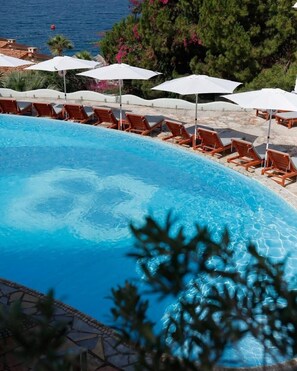 Una piscina con agua cristalina, rodeada de sillones de madera y sombrillas blancas.