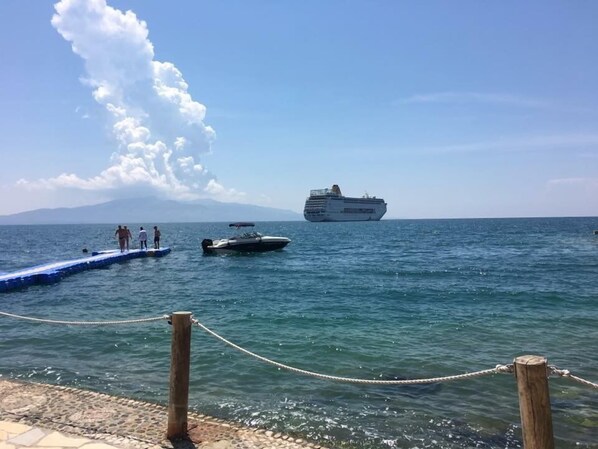 Un muelle con una barandilla de cuerda, un bote pequeño y un crucero al fondo.