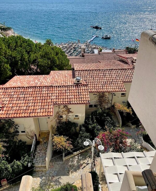 A coastal residential area with terracotta-tiled roofs, a stone pathway, and a view of the sea. - Family Seaview Condo Bougainville Bay (Sarande)