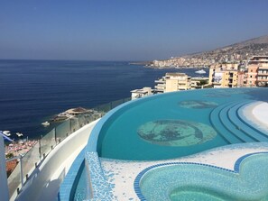 A pool with a clear blue edge and a view of the sea and buildings in the background. - Family Seaview Condo Bougainville Bay (Sarande)