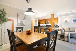Uma cozinha moderna com armários de madeira, sala de jantar com mesa e cadeiras de madeira, e sala de estar com sofá e manta.