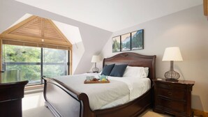 Ein Schlafzimmer mit einem großen Bett, zwei Nachttischen mit Lampen, einem Fenster mit Blick auf Grünflächen und einem Gemälde an der Wand.
