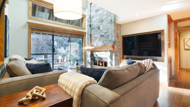 Ein gemütliches Wohnzimmer mit Kamin aus Stein, großen Fenstern und einer bequemen Couch.