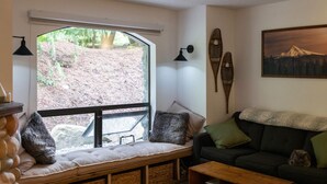 Un salon confortable avec une grande fenêtre, un canapé, un banc et une table basse.