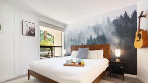 Une chambre à coucher avec un grand lit, une tête de lit en bois, une table de chevet avec une lampe, une guitare et une fresque représentant une forêt.