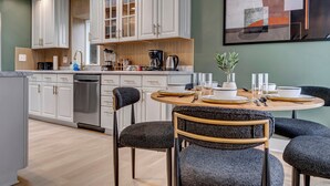 Una cocina moderna con muebles blancos, un comedor con una mesa redonda y sillas, y un cuadro abstracto grande en la pared.