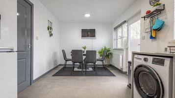 A compact kitchen with a built-in washing machine, a dining area with two chairs, and a flat-screen TV mounted on the wall.