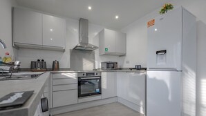 A modern kitchen with white cabinetry, a built-in oven, a microwave, and a refrigerator. - Premium Serviced Accommodation Nottingham-EnsuiteRoom+5mins walk to TrainStation (Nottingham)