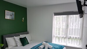 A neatly made bed with white and teal bedding, a green pillow, and rolled towels. A framed inspirational quote hangs on the green wall. - Premium Serviced Accommodation Nottingham-EnsuiteRoom+5mins walk to TrainStation (Nottingham)