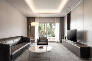 Een moderne hotelkamer met een leren bank, een rond salontafeltje, een flatscreen televisie en uitzicht op het omliggende landschap.