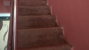 A staircase with a metal handrail and worn steps, leading to a landing with a white wall and a power outlet. - Srikhetra Palace (Puri)