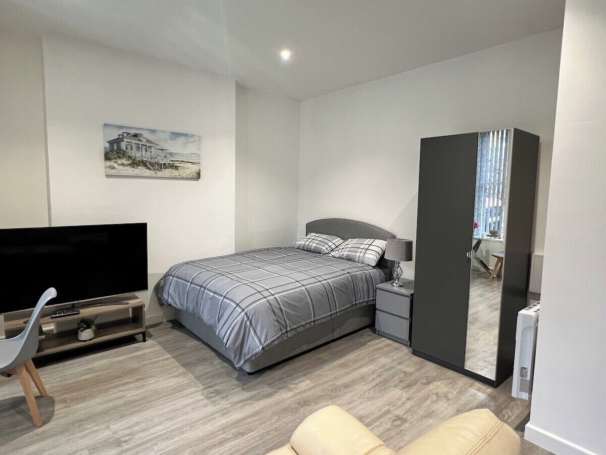 Une chambre à coucher moderne avec un lit, une table de chevet, une télévision et un grand miroir.
