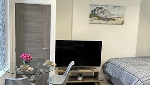 Een moderne slaapkamer met een bed, een televisie, een glazen eettafel met stoelen en een schilderij aan de muur.