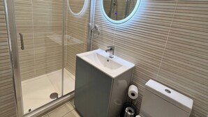 Een moderne badkamer met een douchecabine van glas, een wastafel met spiegel en een toilet.