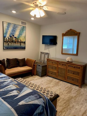 Quarto com cama, sofá, cômoda, televisão e um quadro na parede.