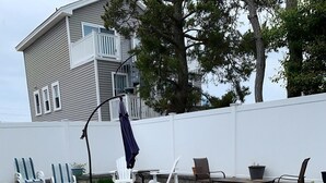 A swimming pool with a metal ladder, surrounded by lounge chairs and tables, with a white building and trees in the background. - Ship Bottom 5 BR Ocean block -Pool (Ship Bottom)