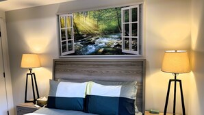 A bedroom with a bed, two bedside tables, a nightstand, a window with a view of a forest stream, and two floor lamps. - 🥇 Black Bears Den, Heated Pool, Hot Tub, Brand NEW! (Canmore)