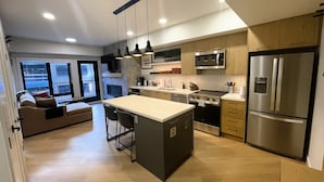 A modern kitchen with a central island, stainless steel appliances, and a view of the city. - 🥇 Black Bears Den, Heated Pool, Hot Tub, Brand NEW! (Canmore)