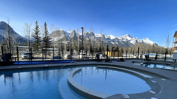A swimming pool with a mountain backdrop, surrounded by trees and a clear sky. - 🥇 Black Bears Den, Heated Pool, Hot Tub, Brand NEW! (Canmore)