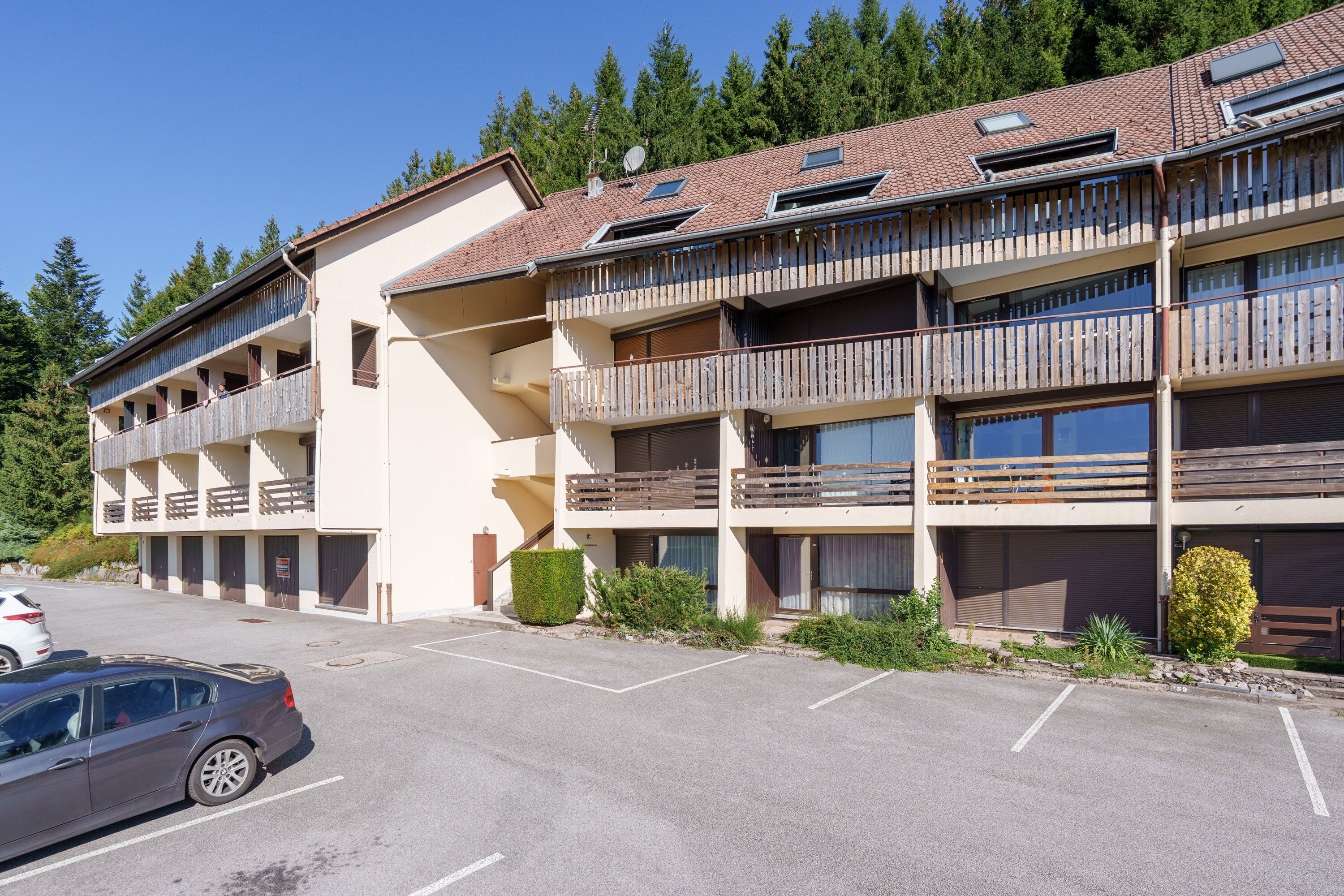 Ein mehrstöckiges Hotel mit Balkonen, einem Parkplatz und einem Wald im Hintergrund.