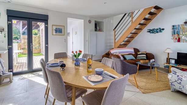 A modern living room with a dining area, a staircase, and a view to the outside. - Gîte des Mouettes - Avec terrasse (Ghyvelde)