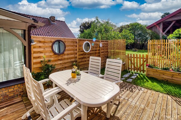 A wooden deck with a table and chairs, surrounded by a wooden fence and a garden. - Gîte des Mouettes - Avec terrasse (Ghyvelde)