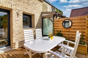 A patio with a white table and chairs, a wooden fence, and a brick wall. - Gîte des Mouettes - Avec terrasse (Ghyvelde)