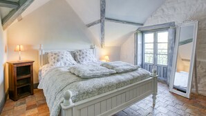 Une chambre avec un plafond en pente, un lit recouvert d’une couvre-lit à motifs, deux lampes de chevet et un grand miroir.