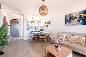 A modern living room with a sofa, coffee table, dining area, and kitchen in the background.