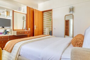 Une chambre à coucher avec un grand lit, une armoire en bois, une télévision et une salle de bain visible à travers une porte ouverte.