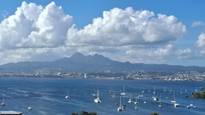 A coastal city with numerous sailboats on the water, a mountain range in the background, and a clear sky.