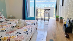 A hotel room with a bed, a desk, a balcony with a view of the sea, and an air conditioning unit.