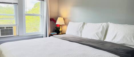 Una habitación de hotel con una cama grande, una mesita de noche con lámpara y una ventana con persianas.