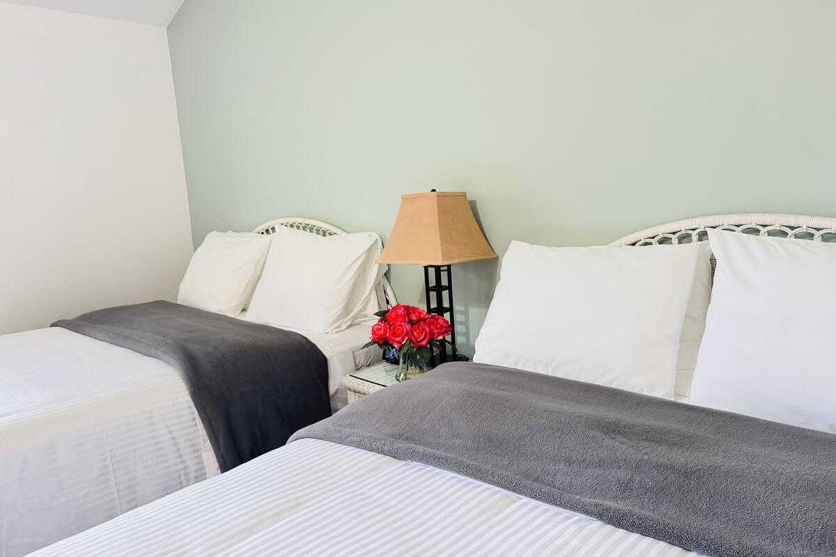 A hotel room with two beds, a nightstand with a lamp, and a vase of red flowers.