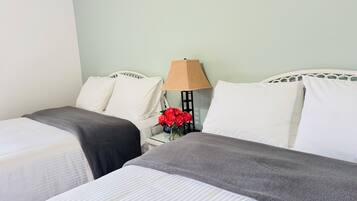 Quarto de hotel com duas camas, uma mesa de cabeceira com abajur e um vaso de flores vermelhas.
