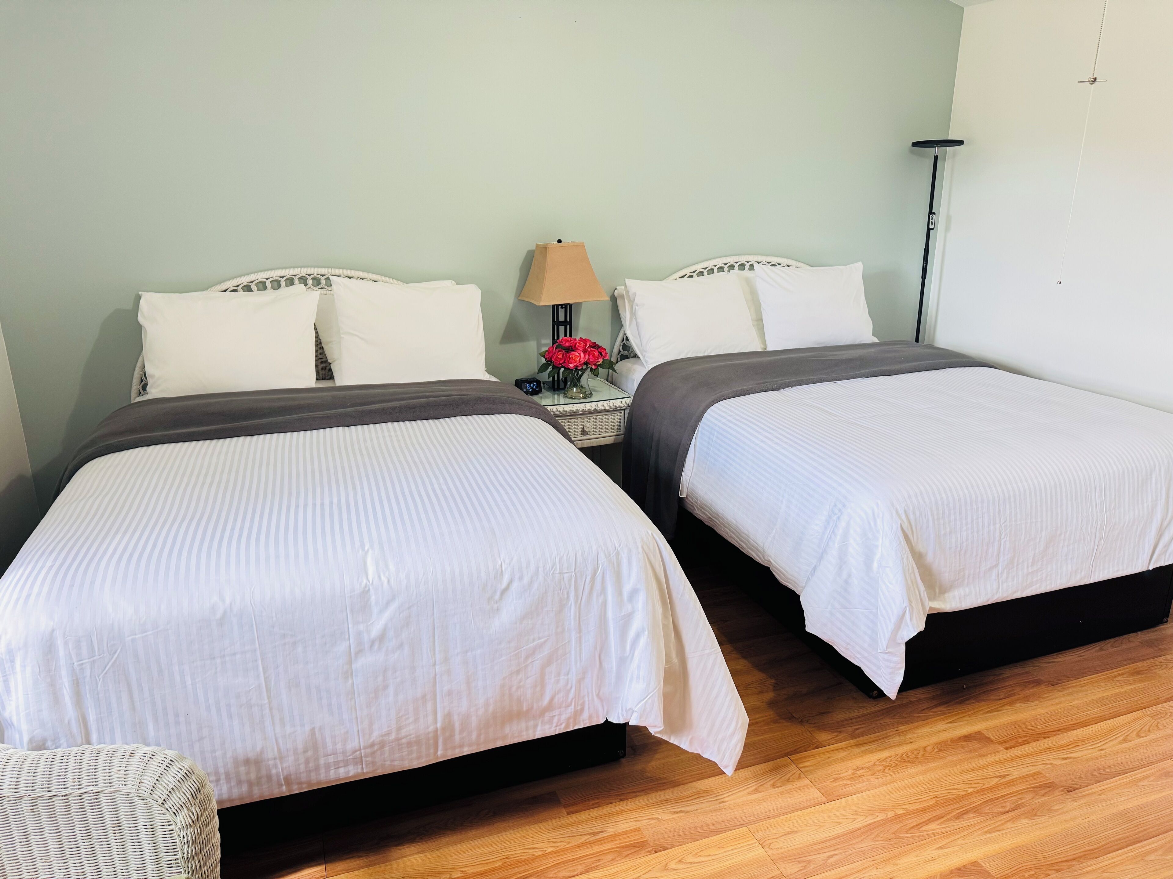 Una habitación de hotel con dos camas, una mesita de noche con lámpara y flores, y una lámpara de pie.