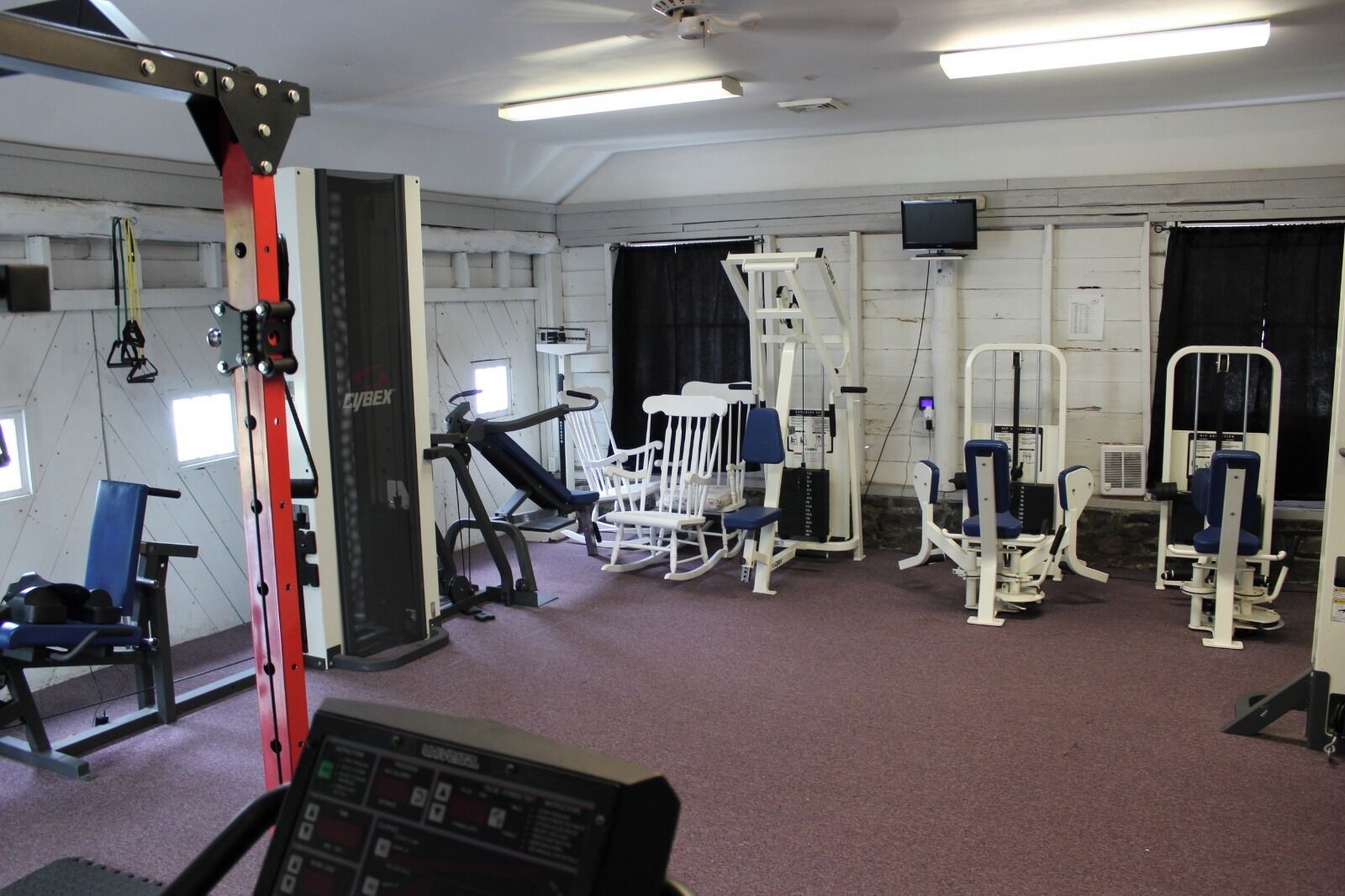 A gym with various exercise machines, a treadmill, and a control panel.